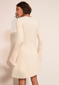 Pitkähiha, ribatulla mekolla pehmeästä kermanvärisestä kankaasta, flare-hihnoilla ja vartalonmyötäisellä yläosalla, joka levenee helmasta. Tuntumaltaan rakennemateriaaliltaan kevyt ja teksturoitu.