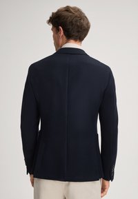 Blazer blu navy con texture, dotato di revers a lancia, doppia apertura posteriore e polsini con bottoni. Tessuto liscio con una vestibilità strutturata.