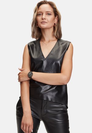 Zwart leren mouwloos topje met een diepe V-hals, een gladde textuur en een getailleerd ontwerp, gecombineerd met zwarte leren broek en een zwart horloge.