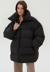 Černá péřová bunda s vysokým límcem, prošívaným designem a oversized střihem. Zapínání na zip a sametová textura zvyšují teplo a styl.