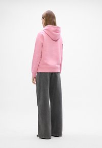 Sudadera con capucha rosa de corte relajado, con puños y dobladillo acanalados. Combinada con unos vaqueros de pierna ancha negros, con un lavado claro y detalles desgastados.
