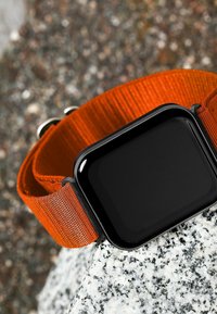 Smartwatch con uno schermo rettangolare nero, dotato di un cinturino in tessuto intrecciato arancione e dettagli in metallo argentato.