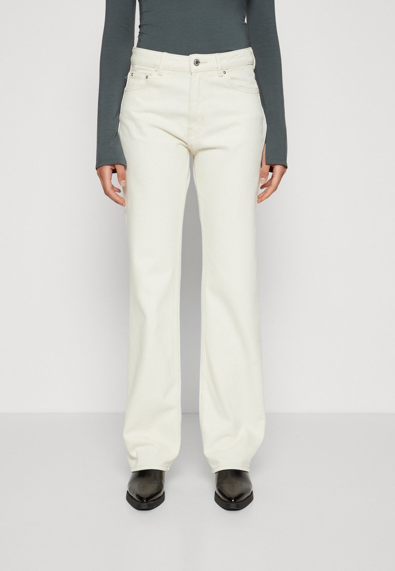 Vaqueros de campana color crema, confeccionados en denim con una textura suave, que cuentan con un botón frontal, lazos para cinturón y bolsillos laterales.