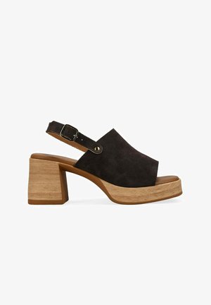 Sandalia negra de ante con puntera abierta, tacón de bloque de madera y correa ajustable en el tobillo con hebilla metálica.