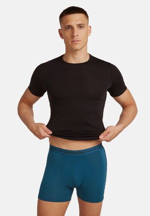 Schwarzes Kurzarm-Crewneck-T-Shirt und türkisfarbene Boxer-Shorts mit einem logoed Bund, die ein enganliegendes Design und eine glatte Textur zeigen.