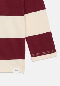 Langermet skjorte med kastanjefargede og kremfargede horisontale striper, laget av bomull, med en sydd kant og en "GAP"-etikett nederst.