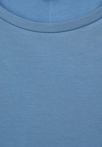 Lähikuva vaaleansinisestä pyöreäkaula-aukko paidasta, jossa näkyy hieno neulekankaan rakenne ja tarkka ompelu kauluksessa.