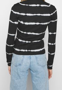 Langærmet top med sort-hvid tie-dye mønster, lavet af ribstrikket stof, tætsiddende design og diskret tekstur langs syningerne.