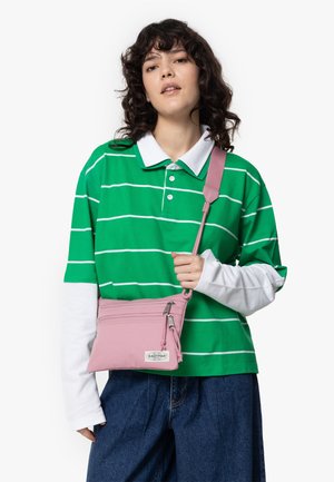 Small pink crossbody bag with two zippered compartments, made of soft fabric. Features a long adjustable strap and a white logo tag.
