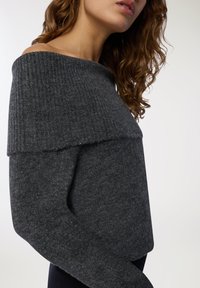 Ciemnoszary sweter bez ramion o prążkowanej teksturze, z długimi rękawami i miękkim wykończeniem. Zaprojektowany z warstwowym wyglądem.