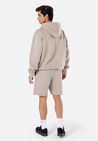 Beige hættetrøje med hætte og ribstrikkede manchetter, parret med matchende beige shorts. Glat tekstur, enkelt design og sorte sneakers.