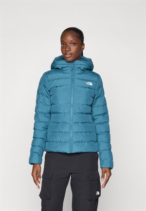 Teal puffer jacket with a hood, featuring horizontal quilted design and a front zipper. Notable logo displayed on the left chest.