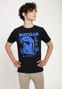 Černé tričko s modrým grafickým designem nahé postavy a abstraktních tvarů, s textem "MATISSE" a odkazy níže.