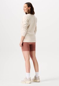 Beige tröja med lång ärm, kombinerad med ribbade, midjehöga, vinröda shorts. Bärs med beige sneakers och vita strumpor.