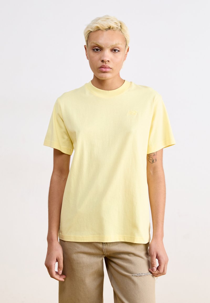 T-shirt en coton jaune clair à manches courtes et col rond. Il présente un petit logo brodé sur la poitrine et une coupe décontractée.