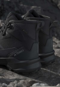 Close-up of black Terrex Gore-Tex hiking boots resting on rocky ground, showing durable design and textured soles for outdoor use.