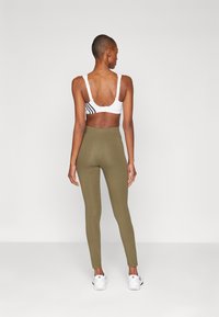 Vit sport-bh med svarta ränder, ihop med olivgröna leggings. Leggingsen har hög midja och en mjuk textur. Vita träningsskor.