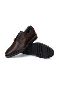 Des chaussures habillées en cuir marron présentent une pointe arrondie, un design à lacets et une semelle en caoutchouc noir texturé avec un motif de crantage.
