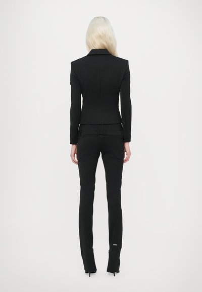 Black tailored blazer and matching trousers, fitted design, smooth texture, wearing high-heeled shoes, subtle logo detail on pants.