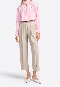 Blusa de rayas rosa claro con cuello alto y lazo, combinada con pantalones de pierna ancha beige y tacones de slingback blancos. Tela suave, ajuste entallado.