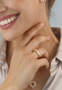 Gold jewelry set featuring a ring with five clear gems, a circular pendant, and matching earrings. Smooth texture, elegant design.