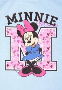 T-shirt azzurro chiaro con una grafica di Minnie Mouse in un vestito blu con un fiocco rosa, accanto alle lettere "M" e "INNIE" in bold con motivi floreali neri e rosa.