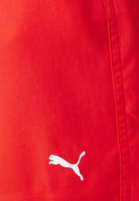 Raudoni sportiniai šortai, pagaminti iš lygaus audinio, su baltu Puma logotipo spaudiniu kairėje apatinėje pusėje. Tvirto dizaino detalė kalba apie šoninius siūlus.