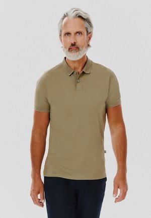 Khaki polo z klasycznym kołnierzykiem, krótkimi rękawami, dwoma guzikami oraz teksturowanym materiałem. Noszony z ciemnymi spodniami.