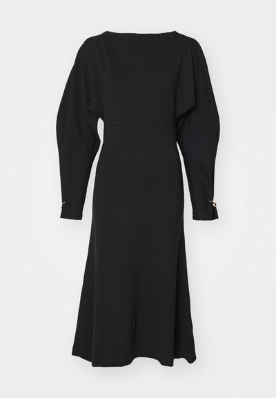 Černé pletené šaty s lodní výstřihem, dlouhými nafouklými rukávy a mírně rozšířeným lemem. Zlaté akcenty na manžetách rukávů.