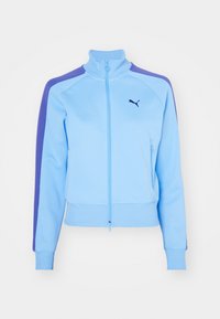 Giacca zip azzurro chiaro con strisce viola sulle spalle, polsini e orlo a coste, con il logo nero Puma sul lato sinistro del petto.