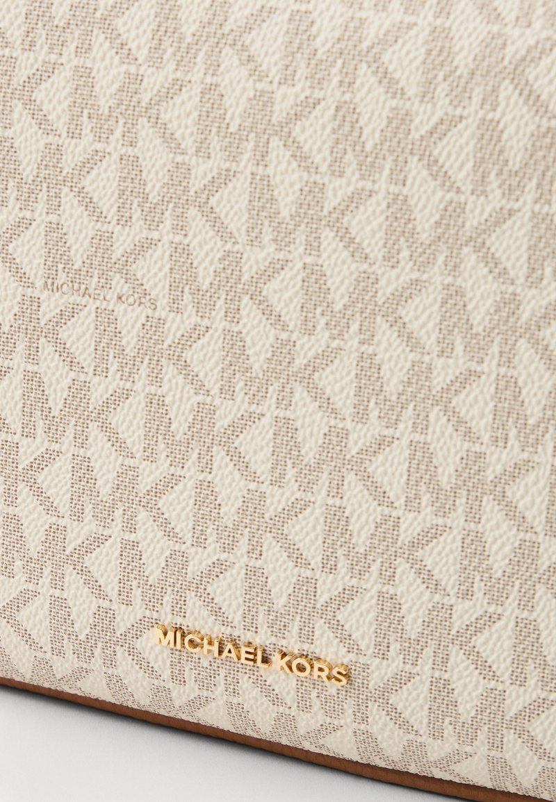 Sac en tissu crème présentant un motif texturé en tout-over de logos entrecroisés "MK", avec une étiquette dorée "Michael Kors" en bas.