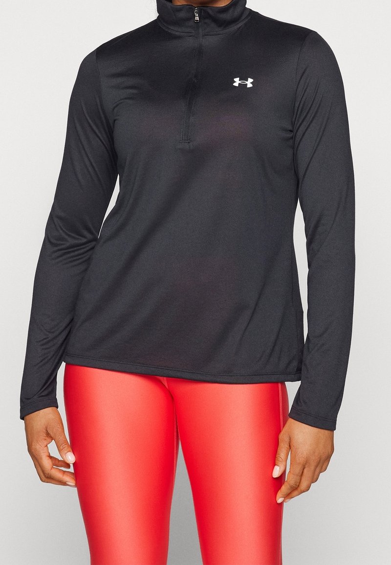 Schwarzes sportliches Langarm-Oberteil mit Reißverschluss am Kragen und Under Armour-Logo auf der linken Brust, kombiniert mit glänzenden roten Leggings.