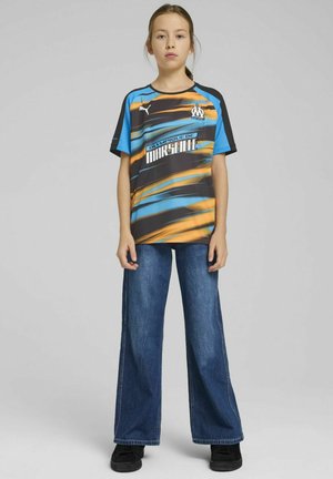 Puma t-shirt met een blauw, oranje en zwart golvend patroon, met "Olympique de Marseille" branding. Gecombineerd met brede blauwe jeans.
