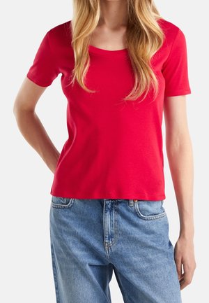 Camiseta roja de algodón con escote redondo y mangas cortas, con un diseño ajustado. Combinada con vaqueros de talle alto en azul claro.