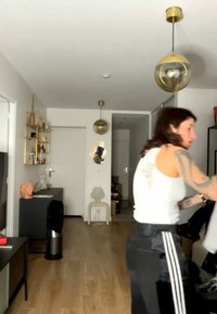 Άτομο με λευκή φανέλα χωρίς μανίκια και μαύρο παντελόνι φτάνει μέσα σε μια μαύρη τσάντα σε ένα μοντέρνο σαλόνι με ξύλινο πάτωμα και χρυσά κρεμαστά φωτιστικά.