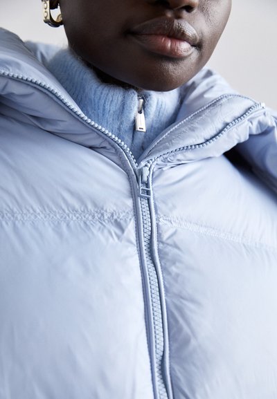 Lichtblauwe pufferjack met een hoge kraag en ritssluiting, met een gladde, glanzende textuur en een comfortabele, blauwe gebreide binnenlaag.