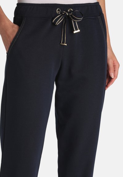 Pantalones deportivos azul marino con bolsillos laterales, cintura elástica y cordón blanco y negro atado en un lazo, combinados con una camiseta blanca.