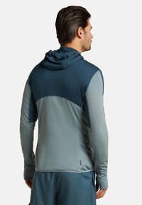 Hoodie med lång ärm i två nyanser av blått; texturerad tyg med släta detaljer; figurnära design med tumhål och en logotagg vid nederkanten.