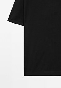 Černé bavlněné tričko s volným střihem, krátkými rukávy a přímým lemem. Tkanina má hladkou texturu.