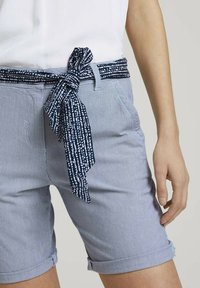 Pantalones cortos a rayas azules y blancas con un cinturón de lazo marino con un patrón de puntos. Dobladillos con puño y bolsillos laterales visibles. Material de algodón.