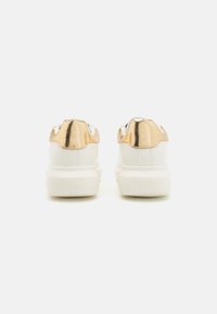 Hvite sneakers med metallisk gull hæl, glatt skinnfinnish og tykk hvit såle, med tradisjonelt snøring.