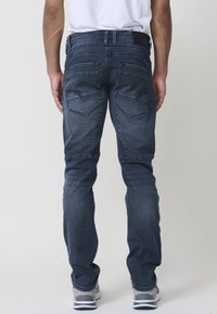 Jeans de mezclilla azul oscuro con un corte recto, que cuentan con dos bolsillos traseros y costuras visibles. Textura suave, diseño minimalista y un ligero desgaste.