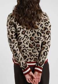 Maglione beige lavorato a maglia con stampa leopardata marrone e nera. Polsini e fondo a righe maroon e bianche a coste. Vestibilità casual e texturizzata.
