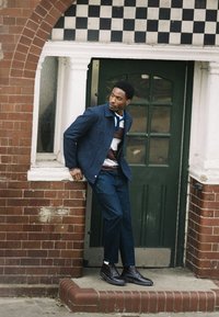 Denimjakke i mørkeblå med to forlommer, kombineret med en stribet polo i brun, hvid og blå, og matchende denimbukser. Sorte støvler.