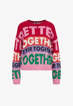 Färggad stickad tröja med vida ärmar; har stor, fet text "TILLSAMMANS" i olika färger: röd, rosa, grön, lila och blå.
