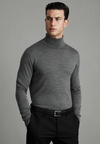 Pulover turtleneck gri dintr-un material moale tricotat, cu un design ajustat, asortat cu pantaloni negri. Textură netedă cu un model subtil de heather.