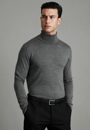 Suéter de cuello alto gris en un material de punto suave, diseño ajustado, combinado con pantalones negros. Textura suave con un sutil patrón jaspeado.