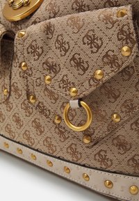 Primo piano di una borsa in tessuto marrone con texture, borchie dorate, chiusura ad anello e un motivo logo impresso ripetuto sulla patta della tasca.