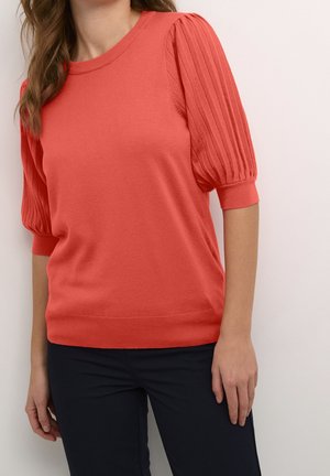 Koralowy sweter z dzianiny z prążkowanymi, bufkami na rękawach, okrągłym dekoltem i dopasowanym dołem. Noszony z ciemnymi spodniami, ukazujący miękką fakturę i żywy kolor.