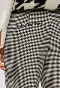 Čierne a biele nohavice s klasickým strihom v houndstooth vzore, s jednou zadnou vreckom a textúrovanou tkaninou.